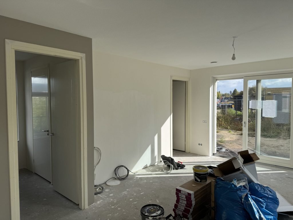 Nieuwbouwwoonkamer tijdens het sauzen, met verfemmers en materiaal op de vloer
