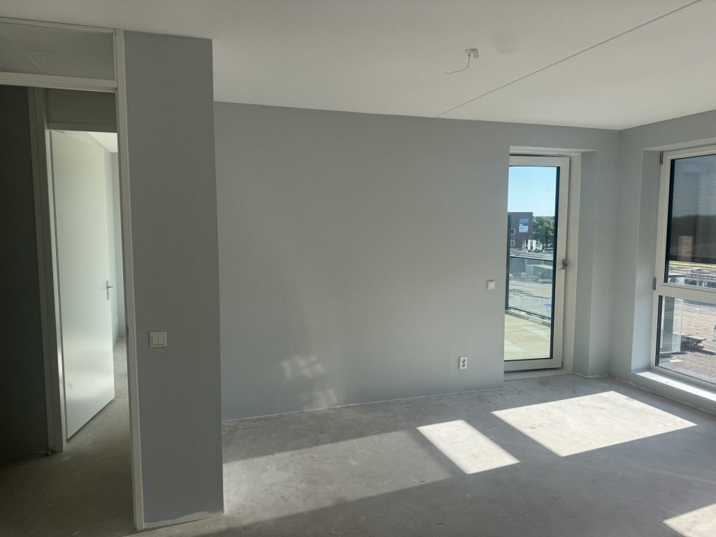 Nieuwbouwappartement met lichtgrijs gesausde wanden en zon op de betonvloer