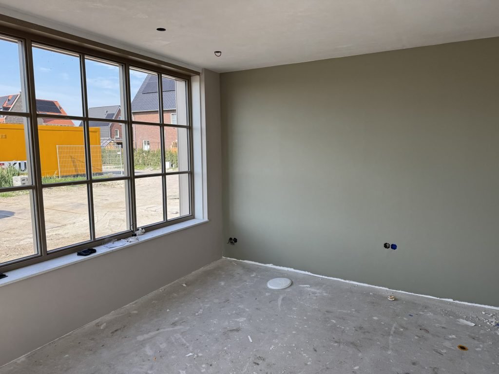 Egaal gesausde wand in een groengrijze tint naast een groot raam in een nieuwbouwkamer