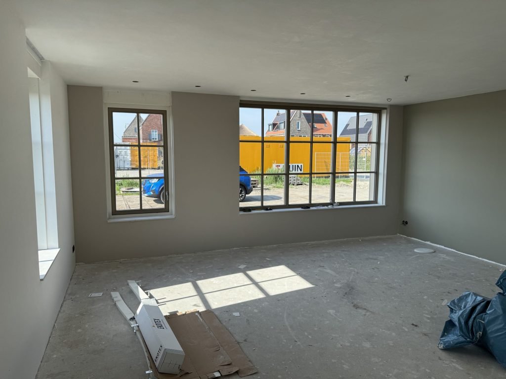 Nieuwbouwwoonkamer met strak gesausde wanden in een warme grijstint en grote ramen