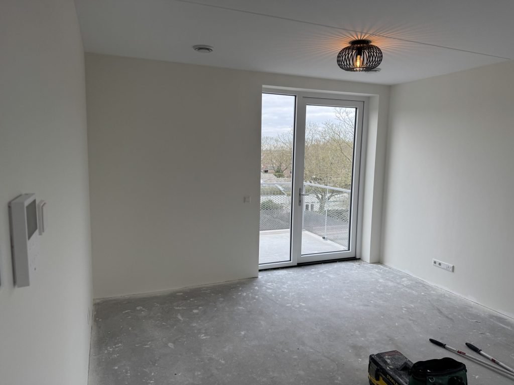 Lege nieuwbouwkamer kort na de oplevering, met strak afgewerkte wanden en openslaande deuren
