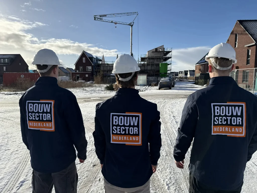 Drie vakmensen van Bouwsector Nederland met witte helm op een besneeuwde nieuwbouwlocatie